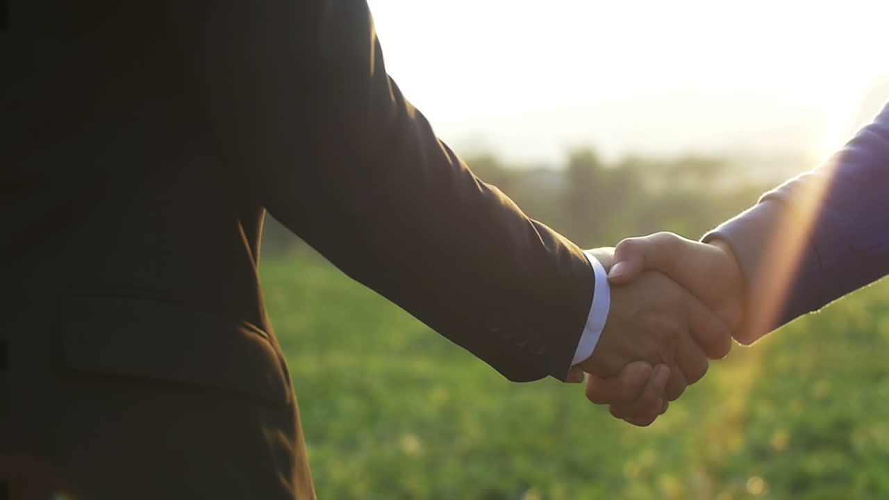 Close Up Of Two Businessmen Shaking Hands On The Farmland