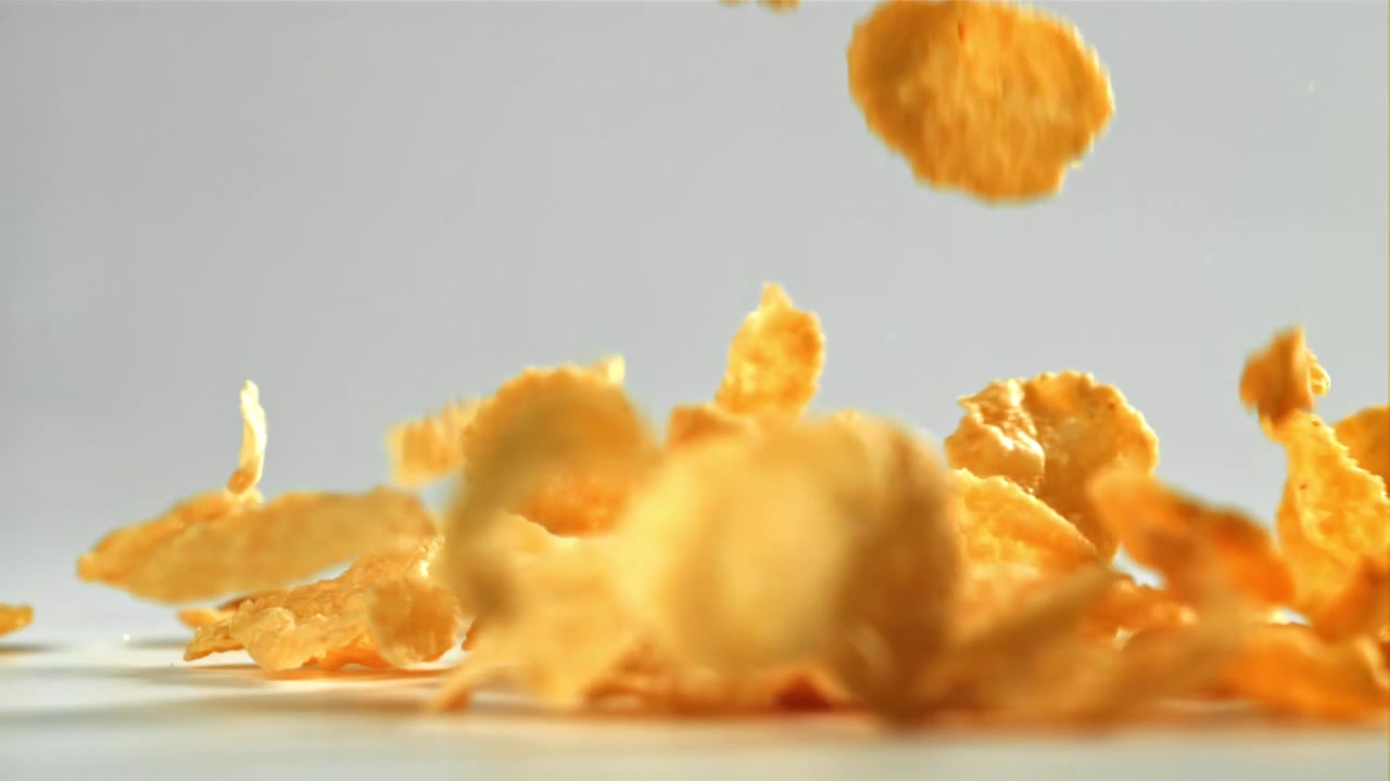 Cornflakes dorati che cadono al rallentatore su uno sfondo bianco