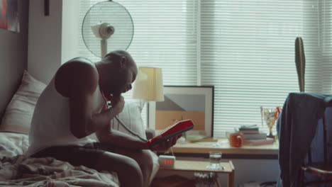 African-American-Man-Sitting-on-Bed-and-Making-Phone-Call-in-Morning