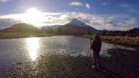 A-wildlife-and-nature-photographer-sets-up-for-a-photoshoot-along-a-river-and-mountains-of-Kodiak-Island-Alaska