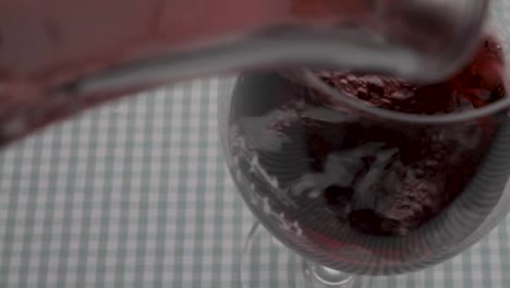 close-up: a static camera captures the process of filling a glass of red wine with a glass decanter, carafe, and a checkered tablecloth