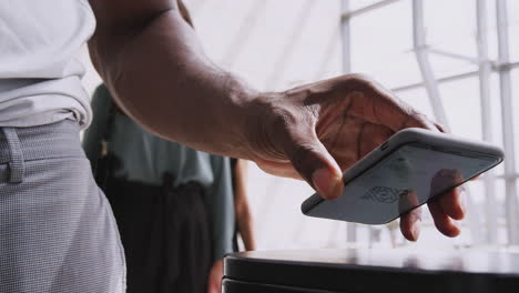 close up of businessman in airport departure lounge scanning e-ticket on mobile phone