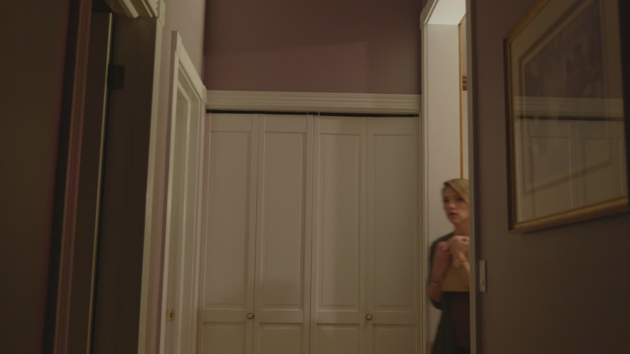A scared woman is seen walking around a door and walking down a hallway.