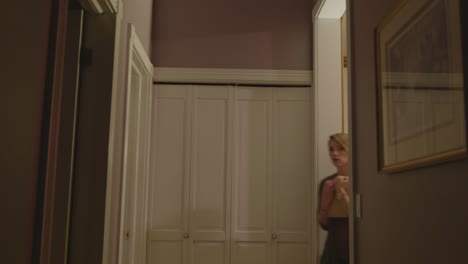 a scared woman is seen walking around a door and walking down a hallway.