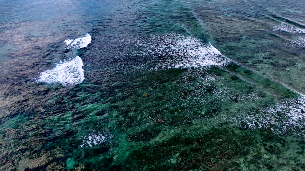 Gentle waves crash over shallow reef of tropical island with clear water, aerial