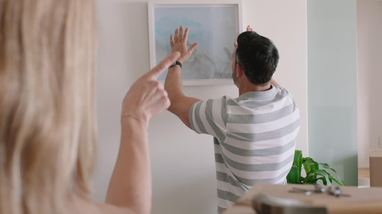 pareja feliz mudándose a una nueva casa dueños colgando fotos decorando la casa juntos disfrutando de un trabajo en equipo exitoso en el apartamento