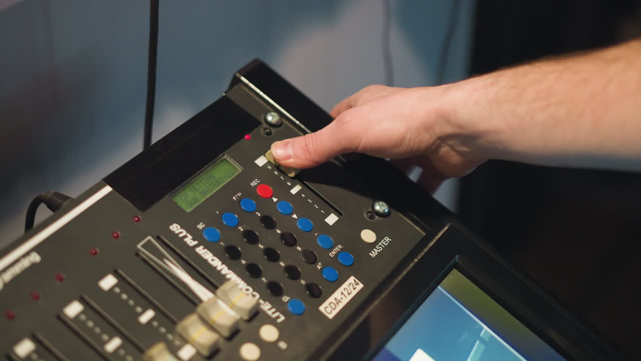 Close-up shot of person adjusting controls on equipment, fingers pressing buttons on digital panel with sliders, screen displaying images, focus on hand performing detailed task in professional studio