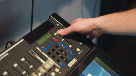 close-up shot of person adjusting controls on equipment, fingers pressing buttons on digital panel with sliders, screen displaying images, focus on hand performing detailed task in professional studio