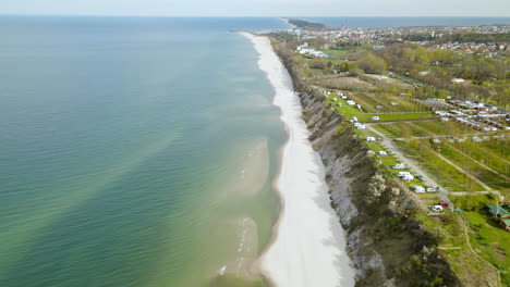 dron lecący wzdłuż bałtyckiej linii brzegowej odsłaniający kemping z licznymi przyczepami kempingowymi na klifie plaży chłapowo i panoramę miasta władysławowa oraz półwysep helski w tle