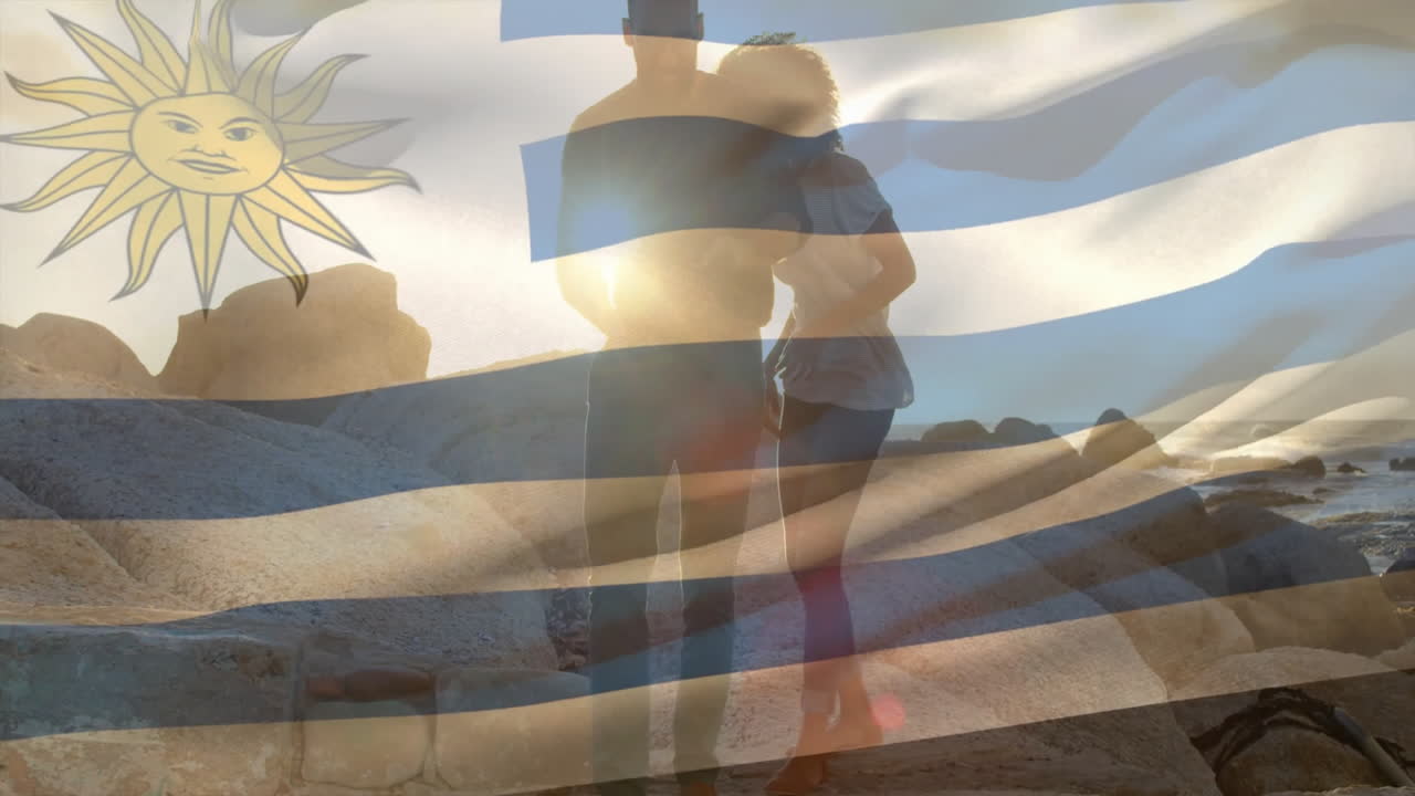 animación de la bandera de uruguay sobre una pareja afroamericana caminando por la playa