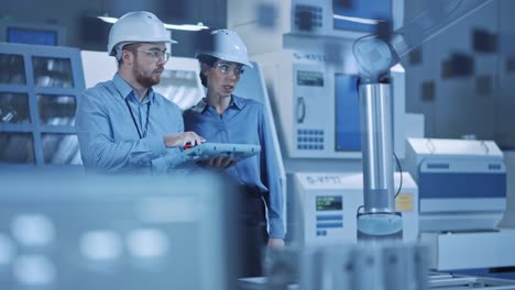 factory workshop: professional female engineer, male machinery operator use industrial digital tablet computer to work and program robot arm for production line. high-tech facility with cnc machines