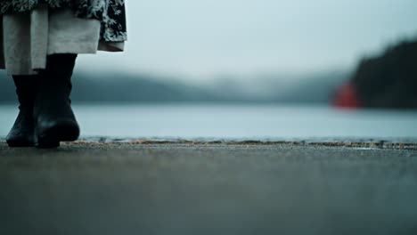 woman in a floral dress and boots by a lake on a foggy day