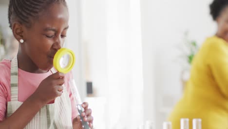 Excited-african-american-girl-looking-at-test-tube-with-magnifying-glass-at-home,-copy-space