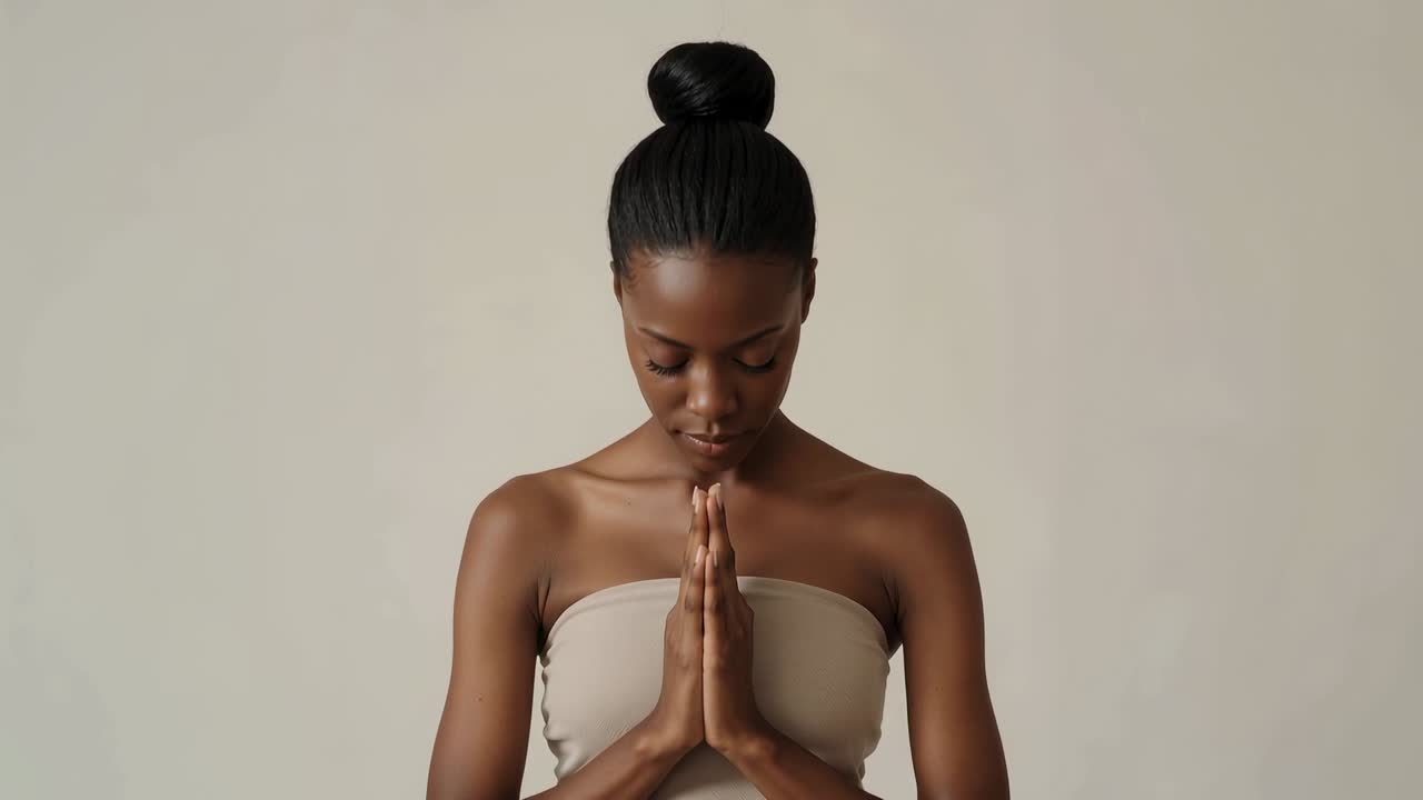 Bowing woman in strapless top lowering chin, eyes closed and pressing palms in studio during prayer