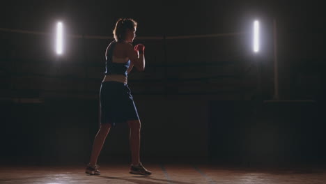 A-beautiful-woman-boxer-trains-in-a-dark-gym-and-works-out-punches-in-slow-motion.-Camera-movement-side-View.-Steadicam-shot