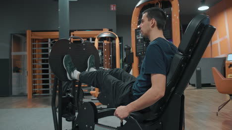 man sits on leg press machine exercising in indoor gym slow motion wide angle