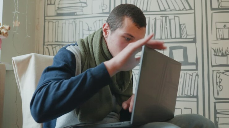 Caucasian man frustrated with laptop, hobbyist confronts malfunctioning hinge and glitching screen in cozy room with patterned bookshelf wall tense gestures, careful inspection with hands