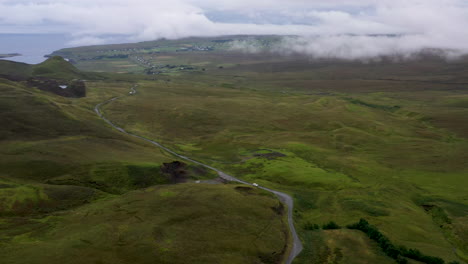 wide drone shot of vehicle on road near quiraing the landslip on the eastern face of meall na suiramach in scotland