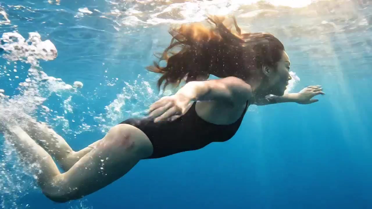 Un nadador elegante se desliza a través de aguas cristalinas, mostrando el arte del movimiento subacuático y la belleza del buceo libre en un entorno sereno.