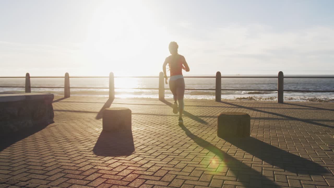 African american woman running on promenade by the sea at sundown
