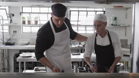 focused caucasian male chef instructing trainee male chefs in kitchen, slow motion