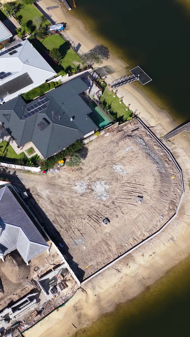 High-angle drone shot reveals residential development progress on a canal waterfront under bright sunlight.