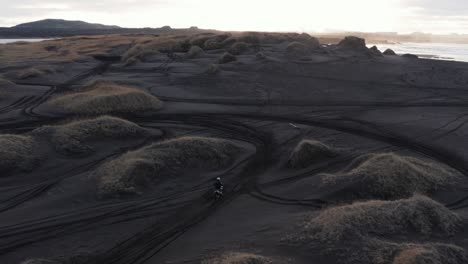 motorbike rider cruising through black sand dunes in iceland, extreme sport, sunrise