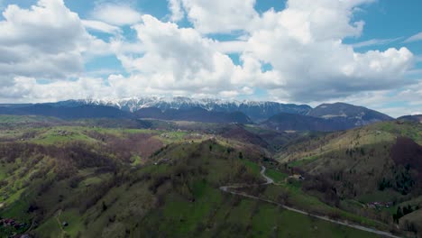 Seitliche-Luftaufnahme-Des-Piatra-Craiului-Gebirges-Mit-Klarem-Blauen-Himmel,-Flauschigen-Weißen-Wolken,-Umgeben-Von-Grünen-Hügeln,-Rumänien,-Siebenbürgen,-Moieciu,-Rucar,-Kleie