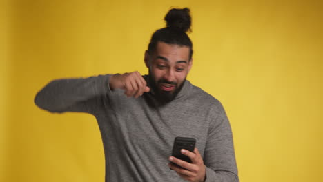 Foto-De-Estudio-De-Un-Hombre-Emocionado-Con-Un-Teléfono-Móvil-Celebrando-Ganar-Dinero-Contra-Un-Fondo-Amarillo