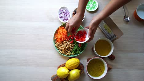 Top-view-shot-making-of-a-salad-adding-tomatoes-carrots-spinach-chick-peas-lemons-onions-nuts-dressing-in-view