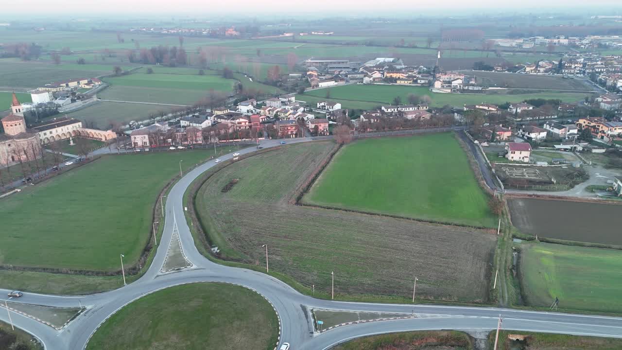Sanctuary of the Blessed Virgin of Mercy rises in Lombardy countryside beside SP415 Strada Paullese, amid green fields, small village houses and winding road traffic, drone panning