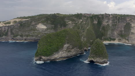 slow pivot shot around a peninsula at kelingking beach with steep cliff on a cloudy day, nusa penida, bali, indonesia.