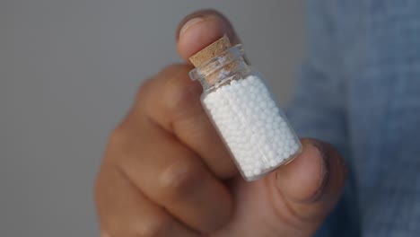 close-up of a hand holding a small glass bottle filled with white pills