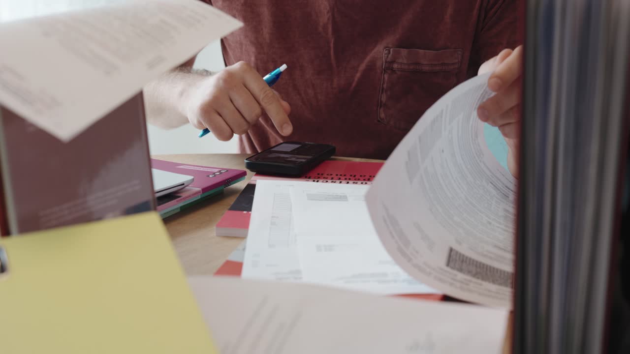 A person reviews tax documents and uses a smartphone and pen at a cluttered desk—suggesting the use of AI tools for accounting or tax preparation