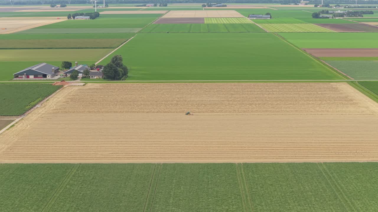 Vista drone di trattore che ara il campo, fienili sullo sfondo, Paesi Bassi
