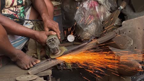 closeup of worker using grinder with no safety equipment barefoot, bangladesh