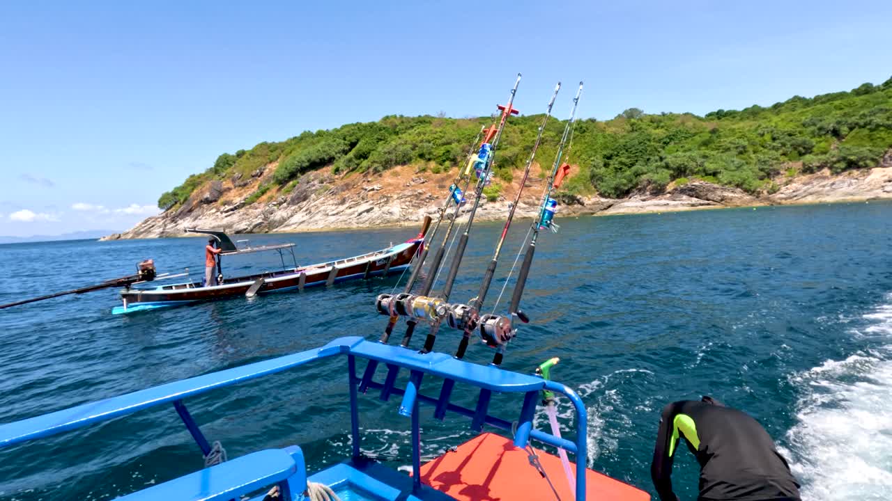 Fishing boats maneuver near lush Phuket shoreline, bright daylight, clear water, handheld camera movement
