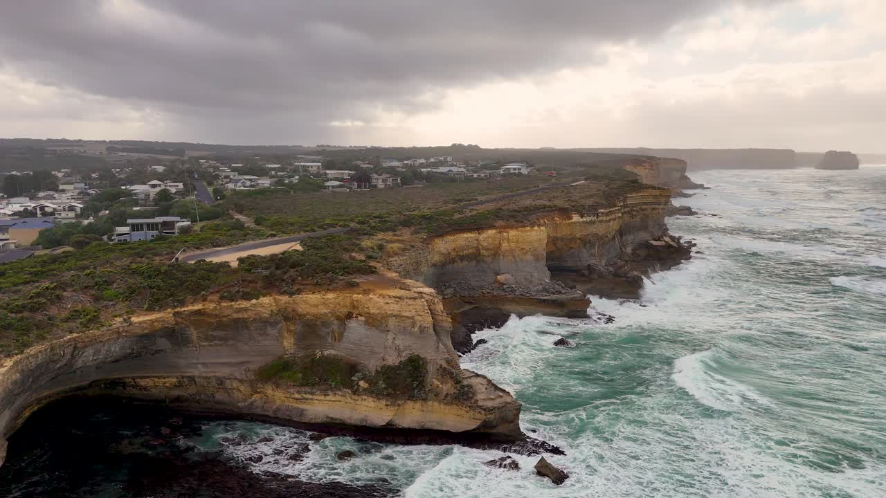 Drone footage captures dramatic cliffs and turbulent seas at Port Campbell, Australia, under overcast skies with dynamic camera movement