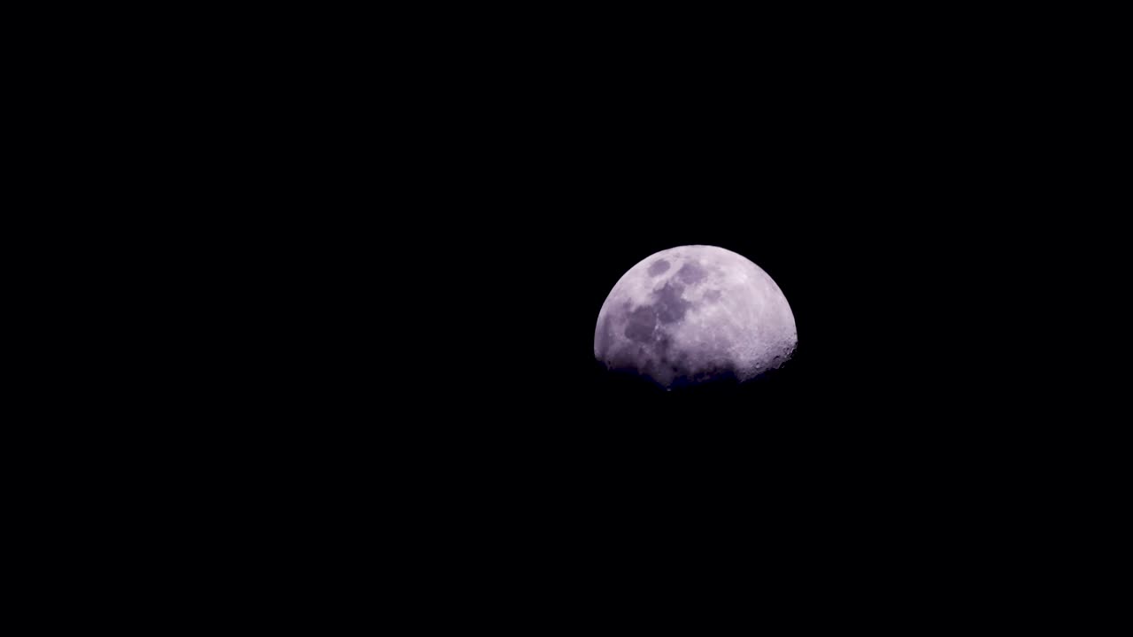 Waxing gibbous moon rising in the darkness of an eerie night as clouds pass in front - zoomed in time lapse