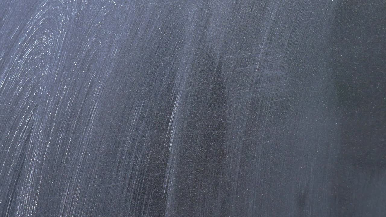 Extreme close up buffing away polish residue from dark grey gar with blue microfibre towel