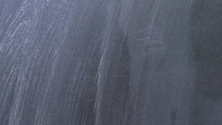 Primo piano estremo di un panno blu in microfibra che rimuove i residui di lucidatura da una gar grigio scuro