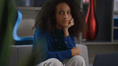 mujer de negocios afroamericana enfocada mirando la cámara sentada en el lugar de trabajo.
