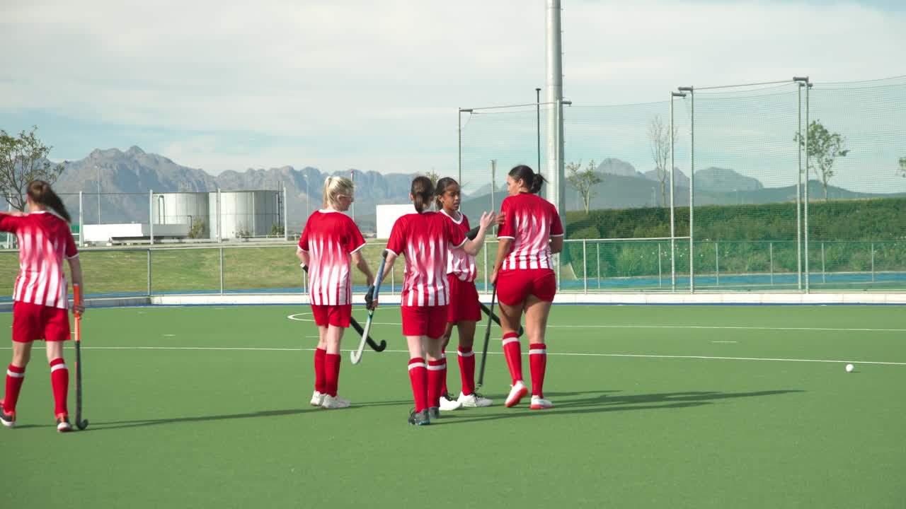 Female hockey team walking on field, preparing for practice under clear sky