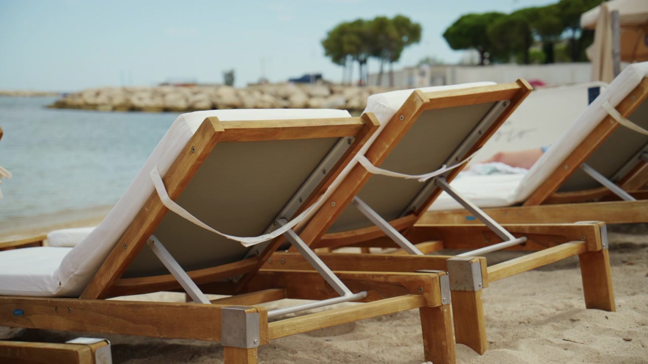 Chaises longues en bois vides avec des coussins reposant sur une plage de sable, offrant un endroit parfait pour la détente estivale au bord de la mer.