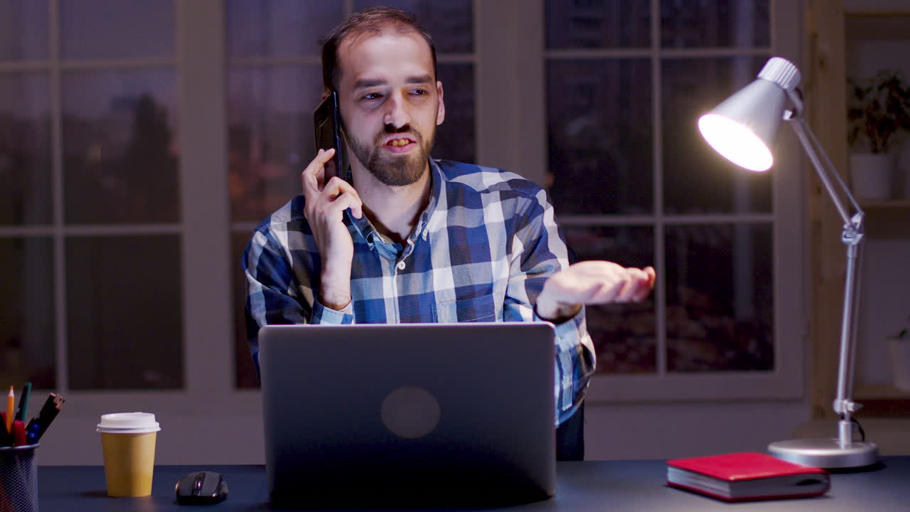 Uomo che parla al telefono mentre usa un laptop alla sua scrivania