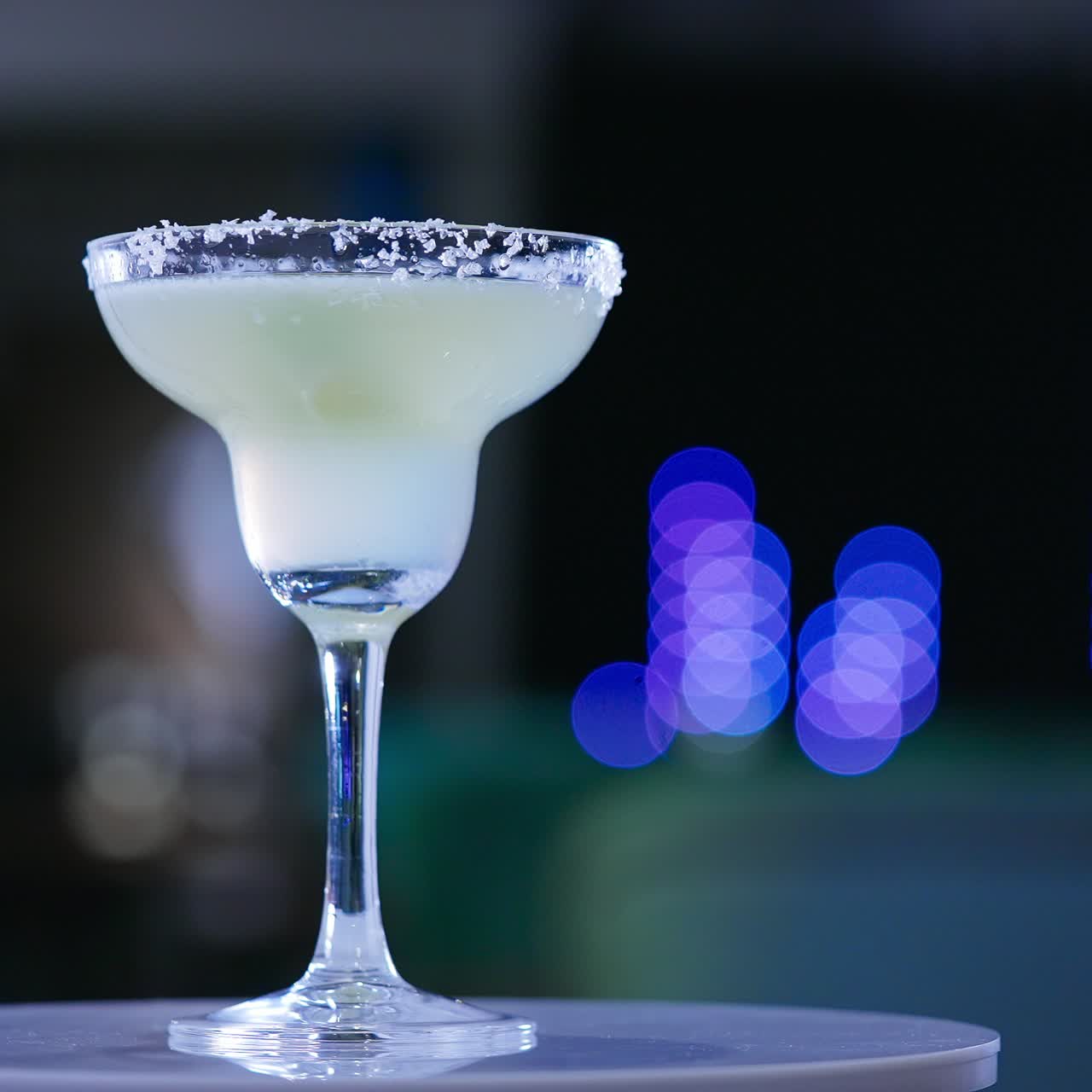 Glass goblet on the little rotating table. Light beverage with a piece of lime inside. Close up. Blurred backdrop