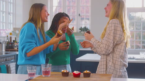 group of teenage girls eating and having fun eating cupcakes in kitchen at home