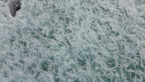 top down aerial view of foamy ocean waves hitting the rocks