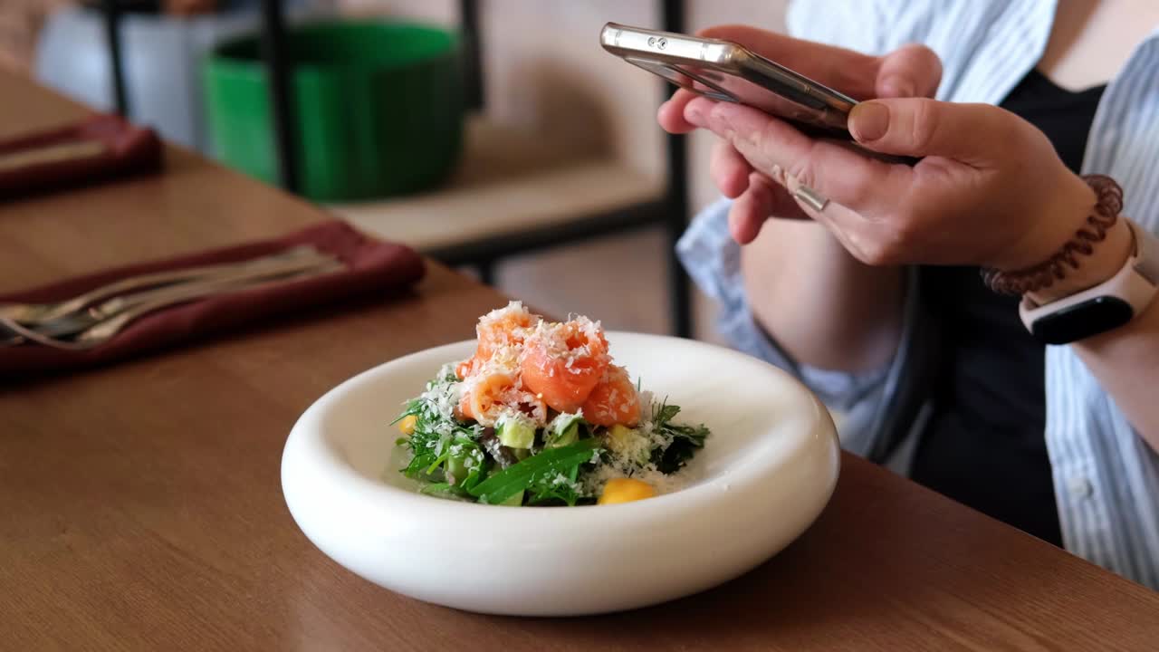 Woman takes picture of avocado and salmon salad on smartphone in restaurant close-up. Slow motion