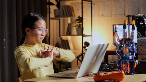 teen asian girl stretching while working about a cyborg hand on a laptop at home